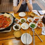 철판 더덕구이와 여러 밑반찬, 동동주가 차려진 야외 테이블