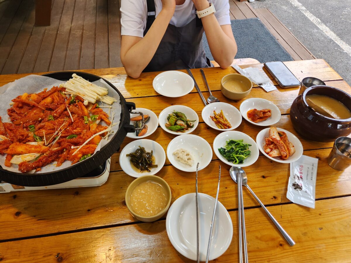 철판 더덕구이와 여러 밑반찬, 동동주가 차려진 야외 테이블