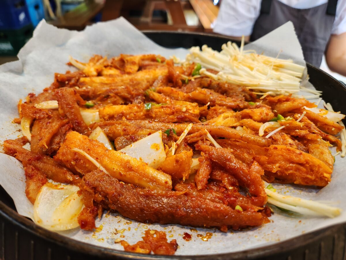 철판 위에 올려진 빨간 양념의 더덕구이와 팽이버섯