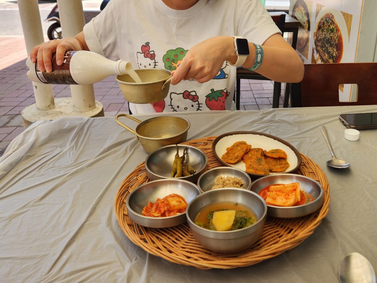 막걸리를 잔에 따르고 있는 모습과 테이블 위의 밑반찬.