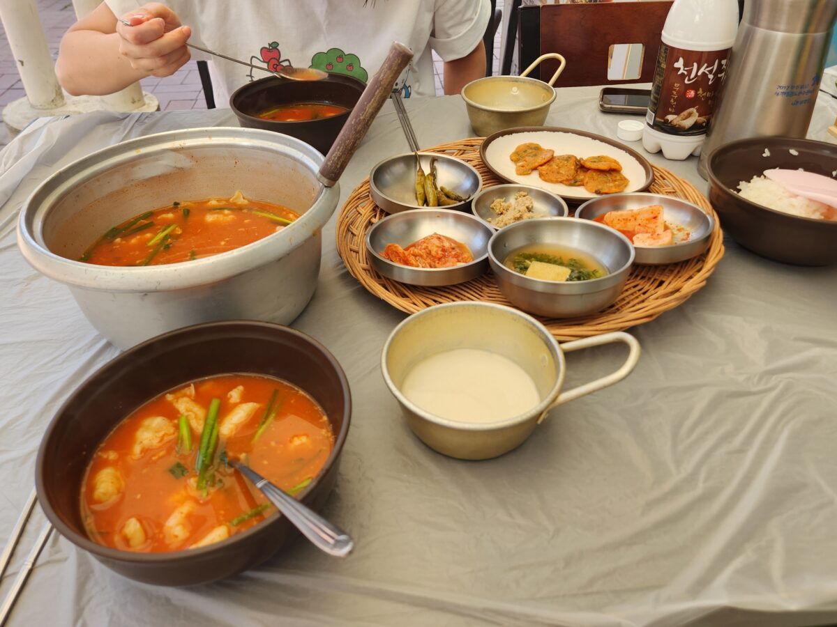 어탕 수제비가 담긴 냄비와 천설주 막걸리, 밑반찬이 차려진 테이블.