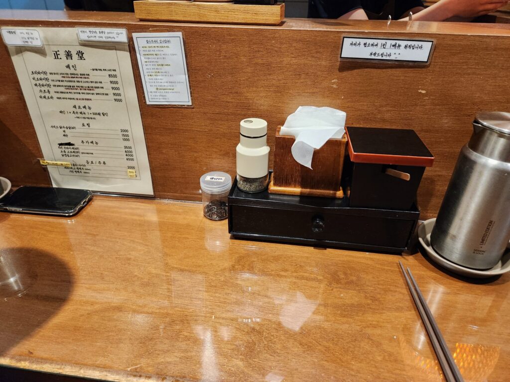 정선당 매장 내부의 우드톤 바 테이블과 메뉴판, 정갈하게 정리된 식기류.