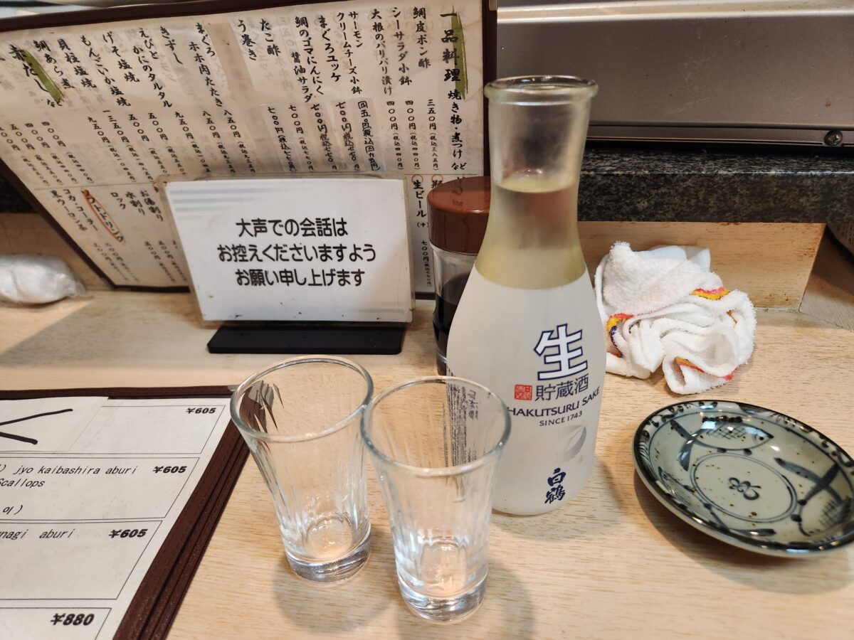 테이블 위에 놓인 하쿠쯔루 사케 병과 잔