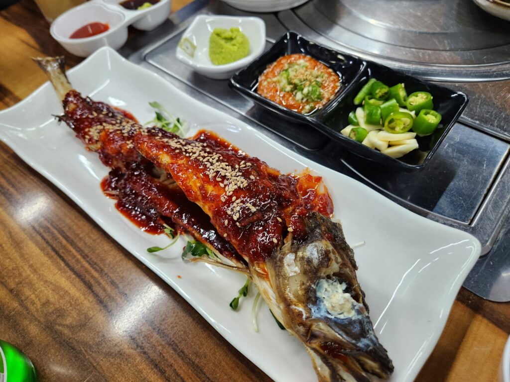 양념장이 올려진 코다리 구이와 유린기, 마늘과 고추, 쌈장 등 횟집 기본 양념 구성.