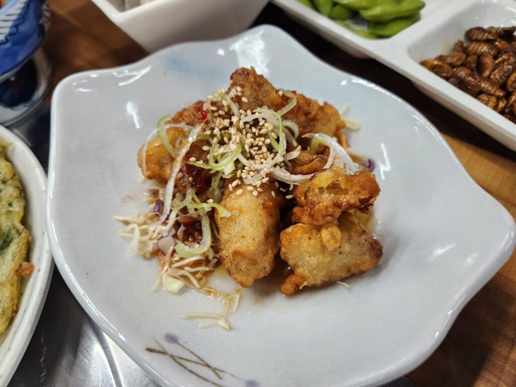 접시에 담긴 닭고기 유린기와 그 위에 올려진 파채와 깨가 확대된 모습.