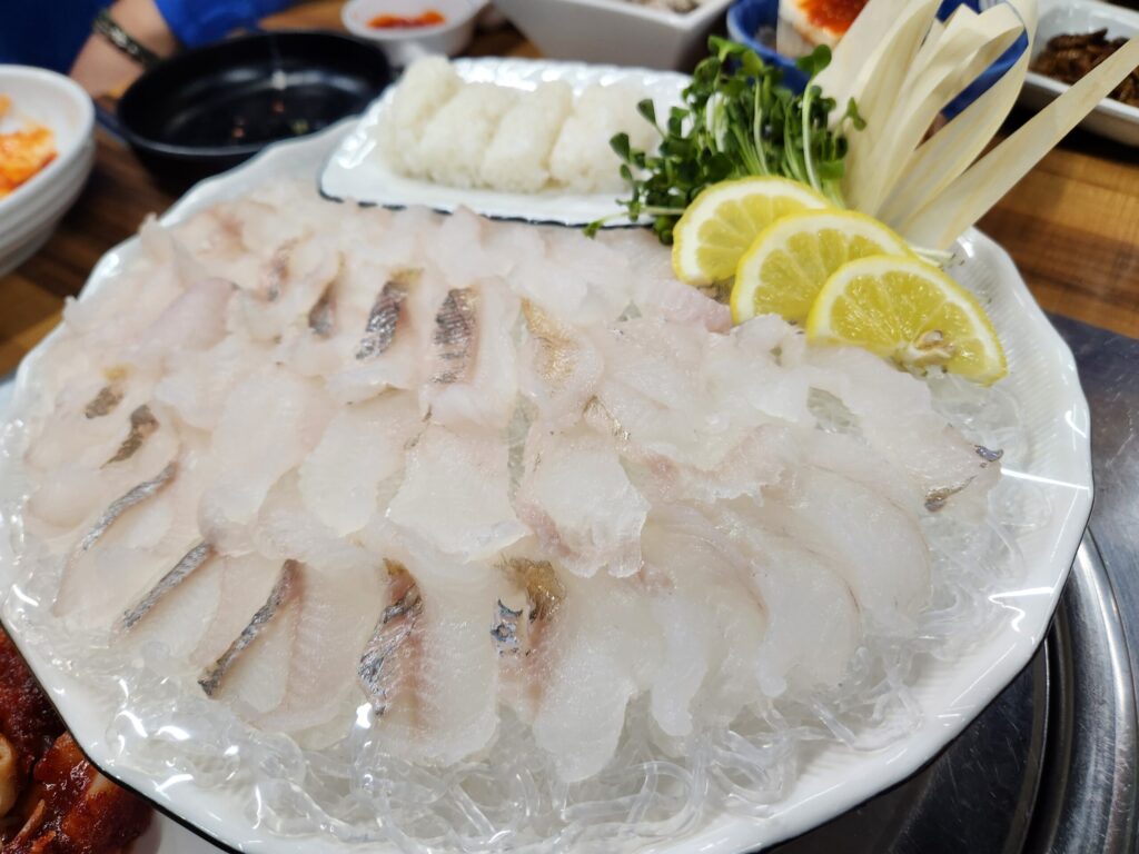 얼음 위에 정갈하게 담긴 고랑치 회 접시와 초밥용 밥, 무순, 레몬이 차려진 모습.