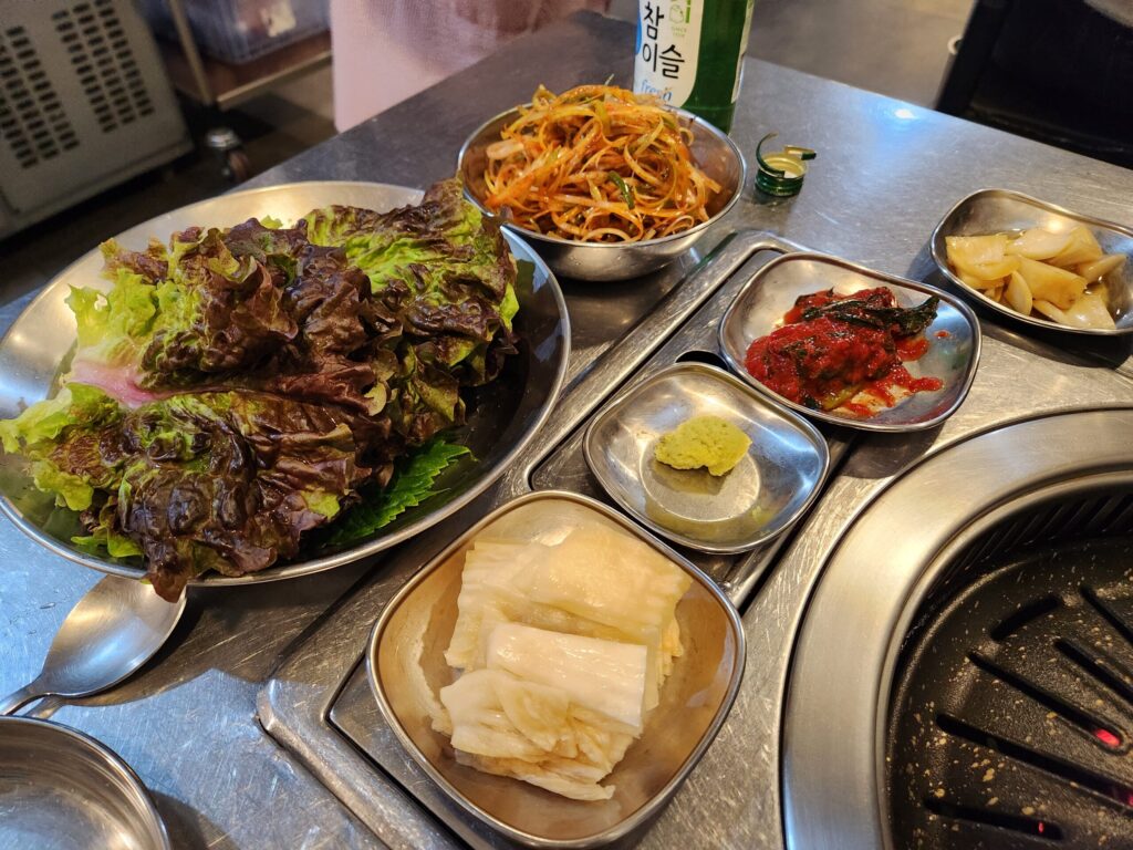 쌈채소, 파무침, 갓김치 등 다양한 밑반찬이 차려진 테이블 세팅.