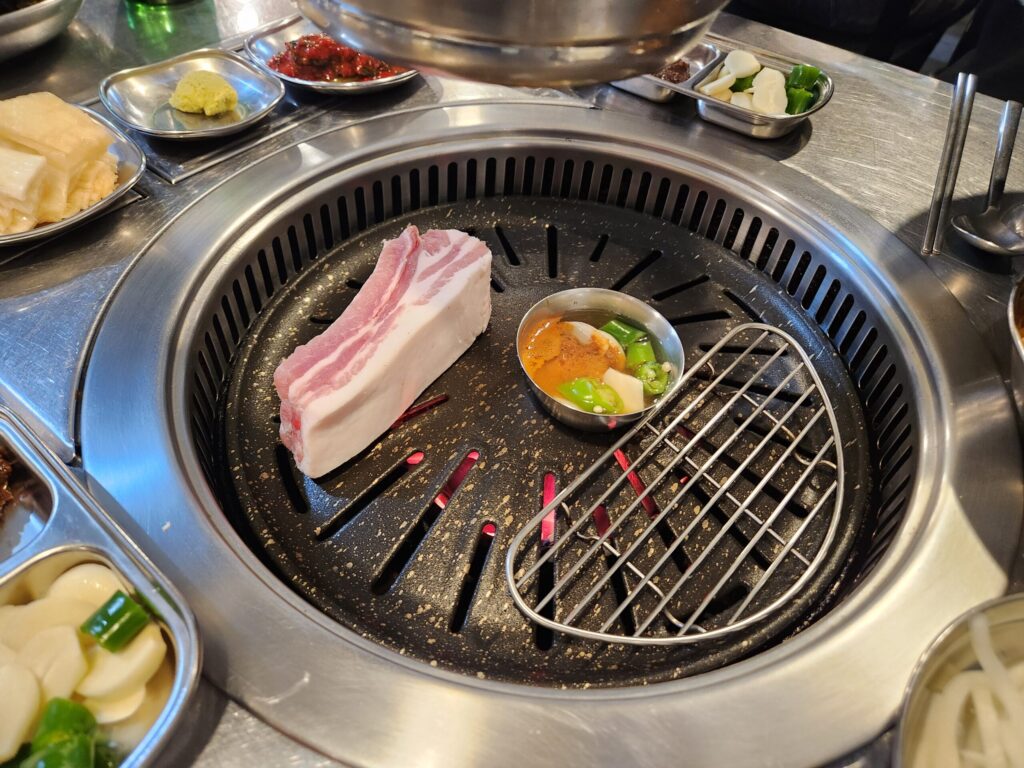 불판 위에 올려진 고기 한 점과 멜젓 소스.