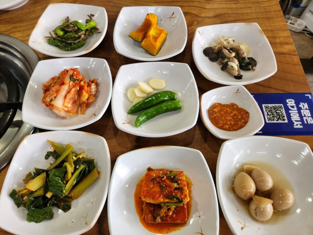 테이블 위에 차려진 버섯나물, 두부조림, 메추리알 등 다양한 밑반찬.