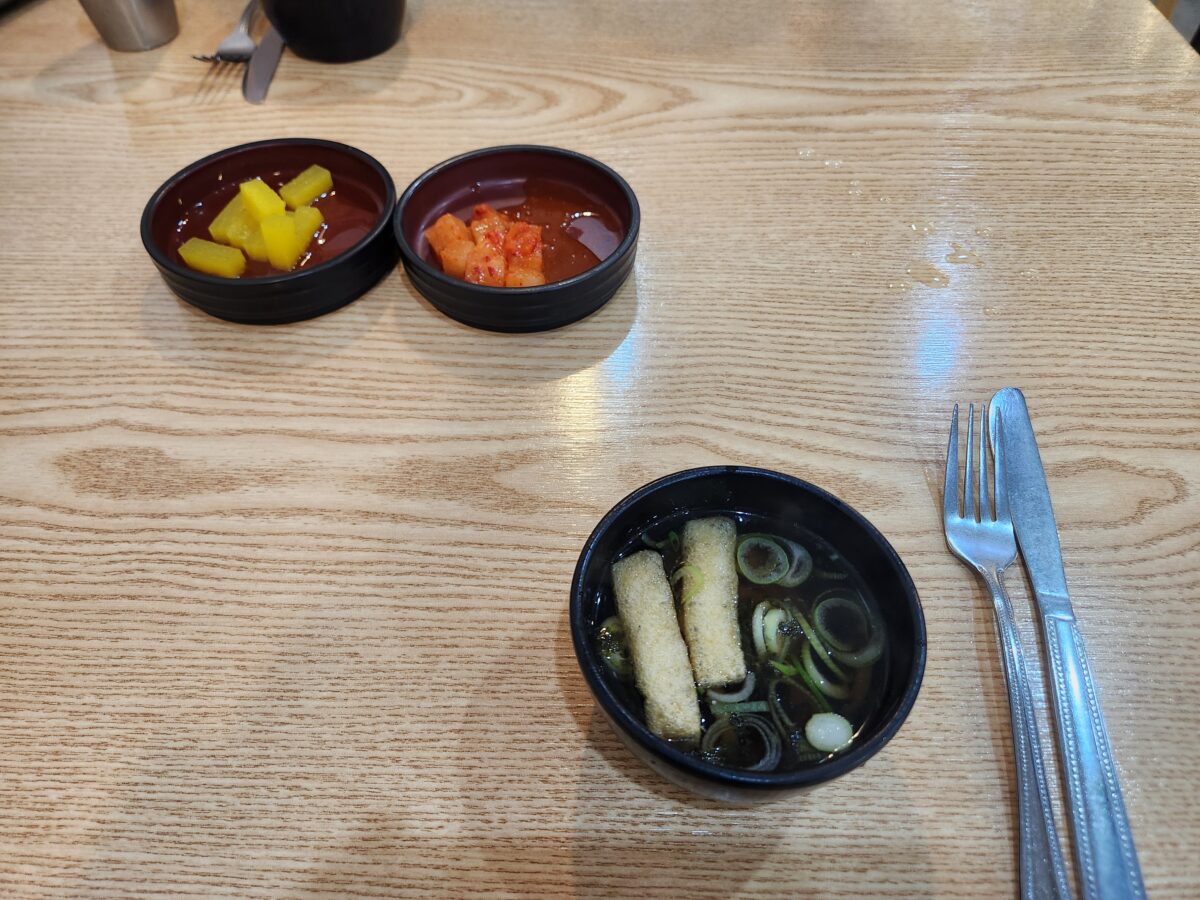 기본 반찬으로 제공된 단무지, 김치, 그리고 우동면이 살짝 들어간 국물 그릇들.