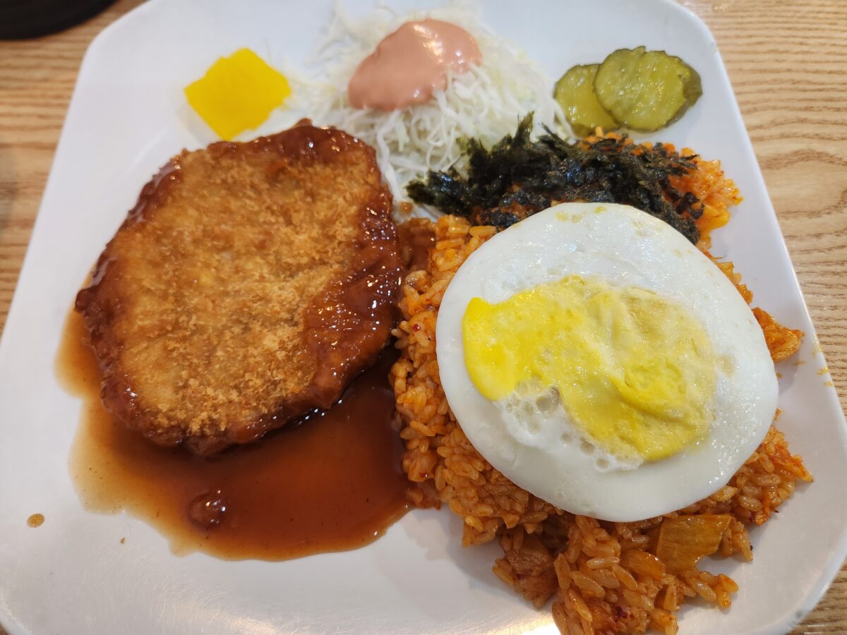 접시에 담긴 돈까스 한 덩이와 계란후라이가 올라간 김치볶음밥, 양배추 샐러드가 놓여 있음.