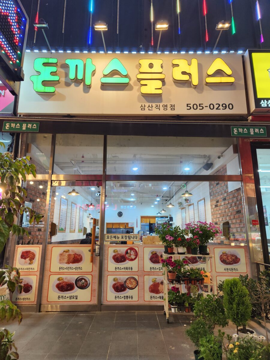 다양한 메뉴 사진이 붙어있는 돈까스플러스 가게 입구 전경.