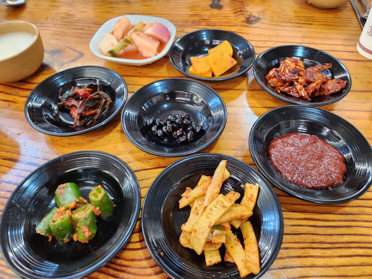 여러 개의 검은색 접시에 정갈하게 담긴 밑반찬들과 순무김치.