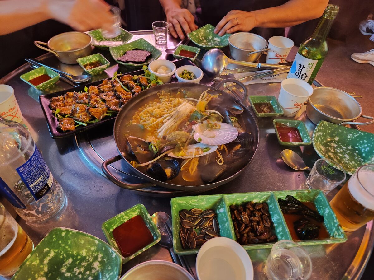 미더덕회와 해물라면, 소주와 맥주 등 다양한 밑반찬이 놓인 식당 테이블의 전체적인 모습.