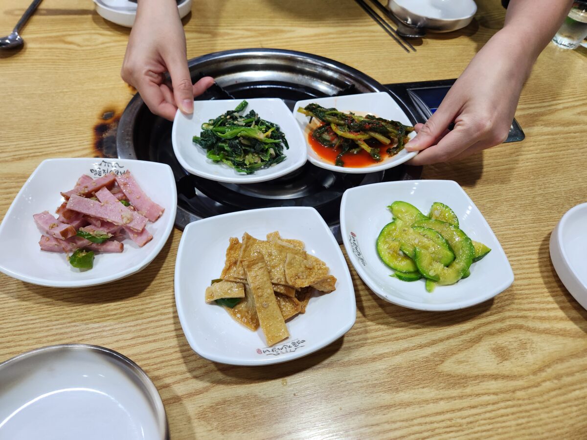 김치, 나물, 햄, 어묵 등이 담긴 기본 반찬 접시들.
