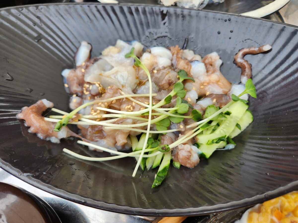 검은 접시에 담긴 잘게 썰린 산낙지와 채소.