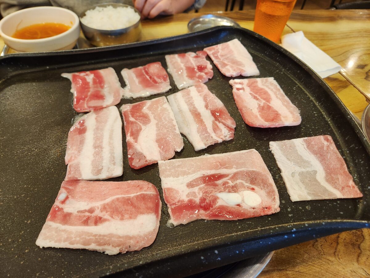 불판 위에 나란히 올려진 냉동 삼겹살 여러 점.