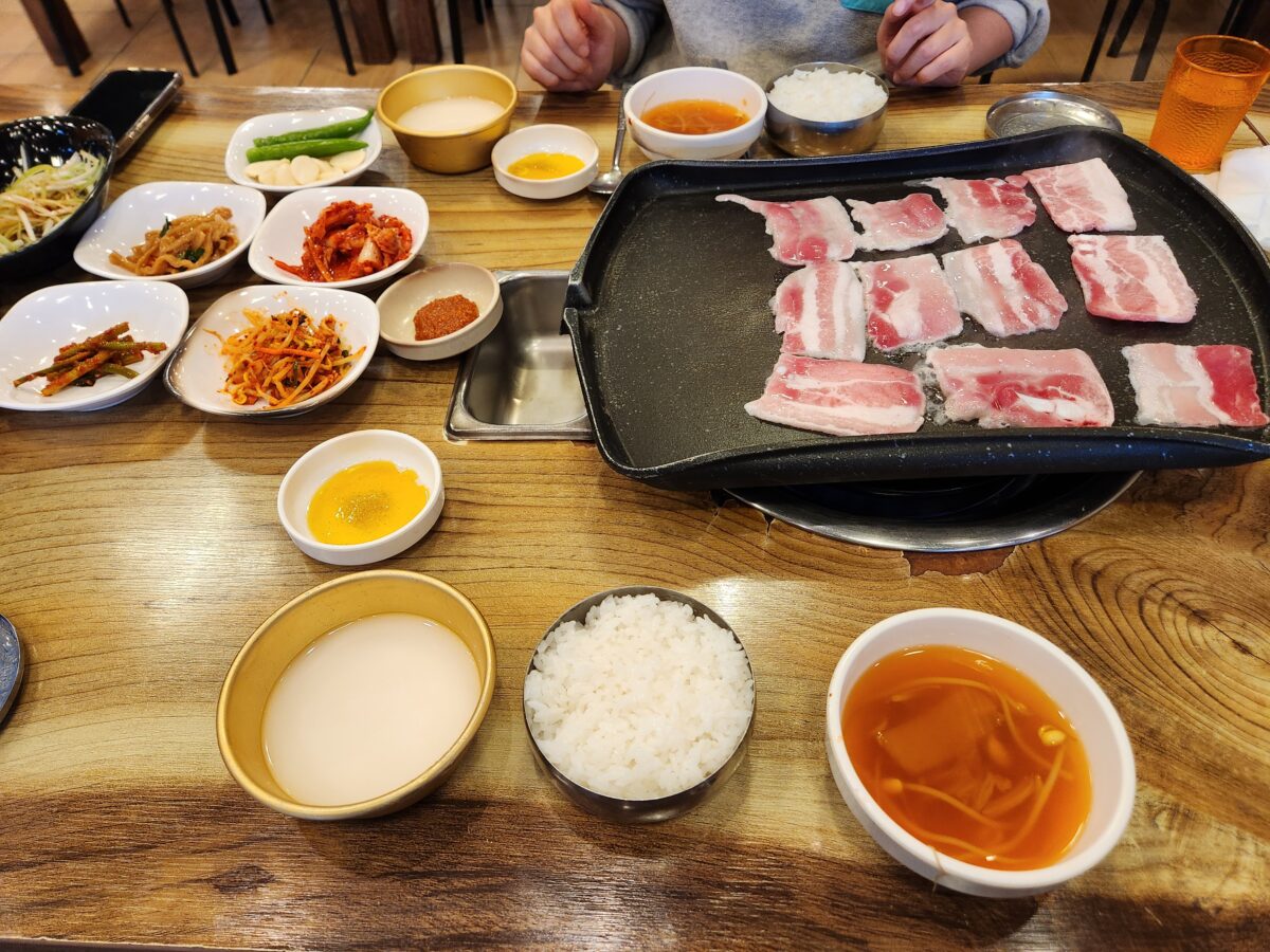 냉동 삼겹살, 밥, 콩나물국, 각종 밑반찬이 차려진 전체 테이블.