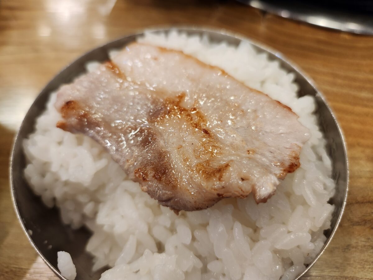 흰 쌀밥 위에 구운 냉동 삼겹살 한 점이 올려져 있는 모습.