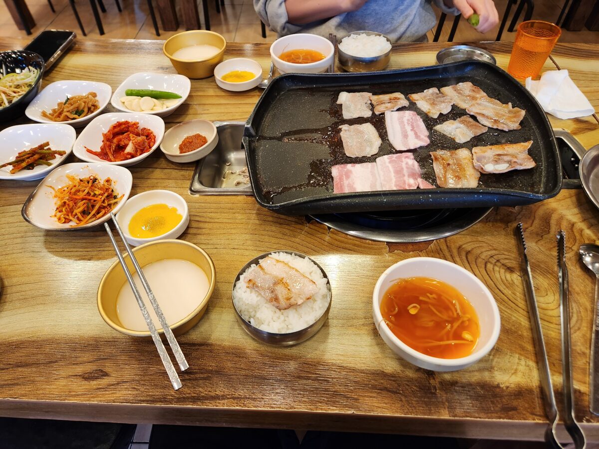 불판 위 고기와 각종 밑반찬, 밥, 막걸리가 놓인 상차림.