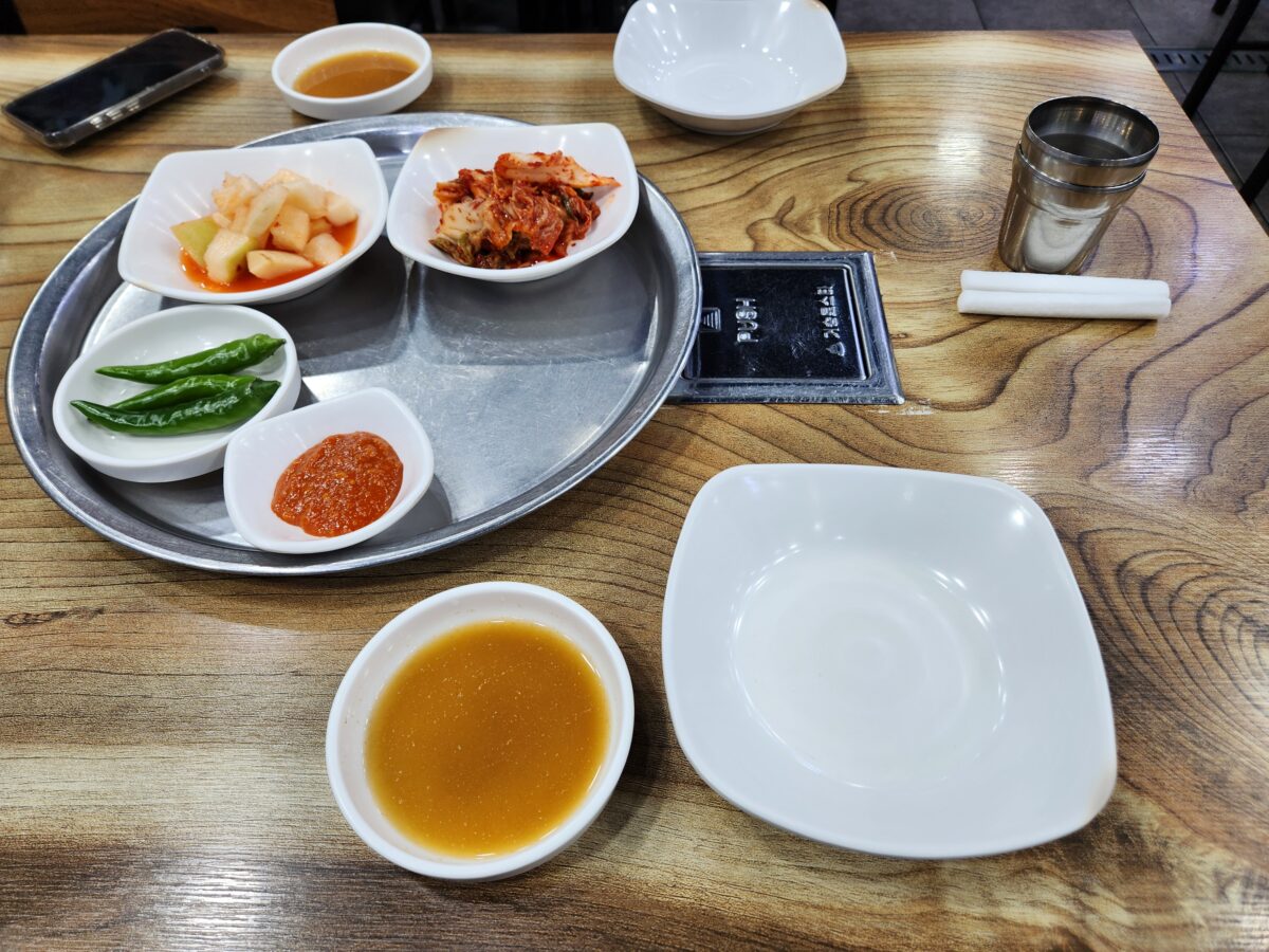 테이블 위에 김치, 깍두기, 고추, 쌈장이 담긴 접시들이 정갈하게 놓여 있음.
