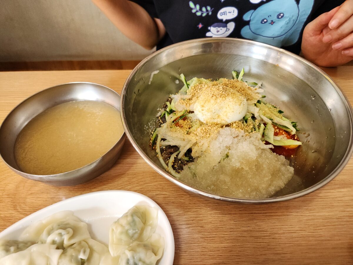 테이블 위에 놓인 비빔냉면과 별도로 제공된 육수, 물만두 접시가 포함된 전체 상차림.