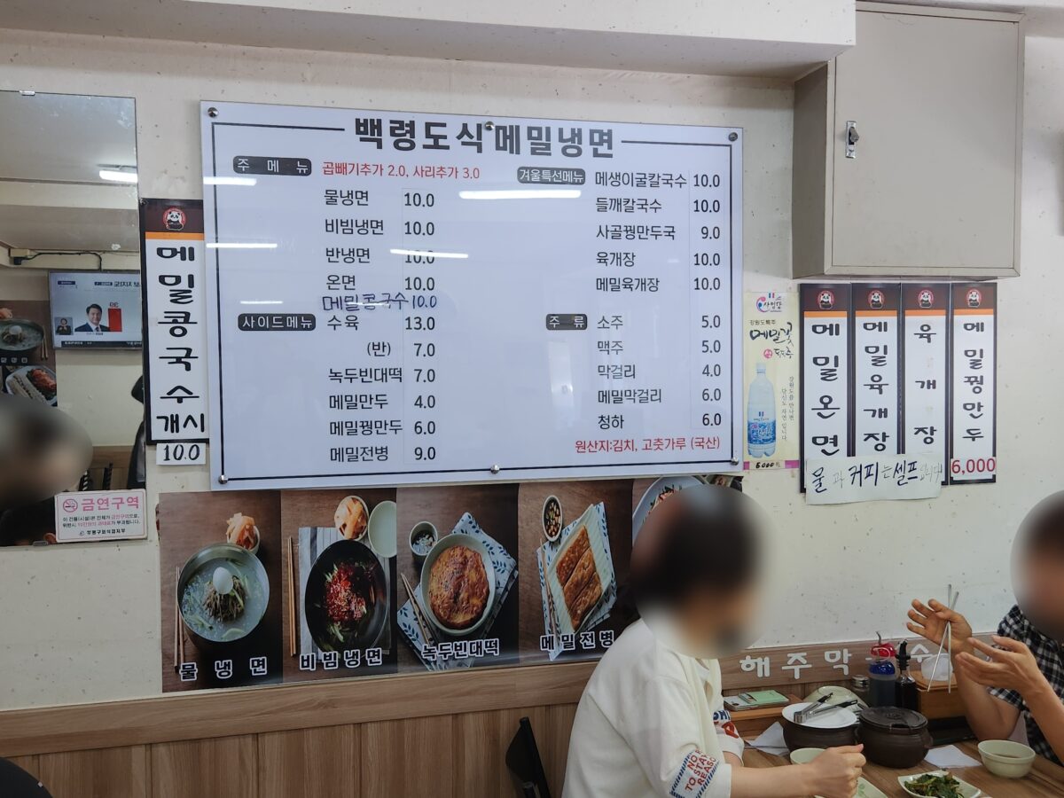 해주막국수 내부의 메뉴판과 식사 중인 손님들의 모습.