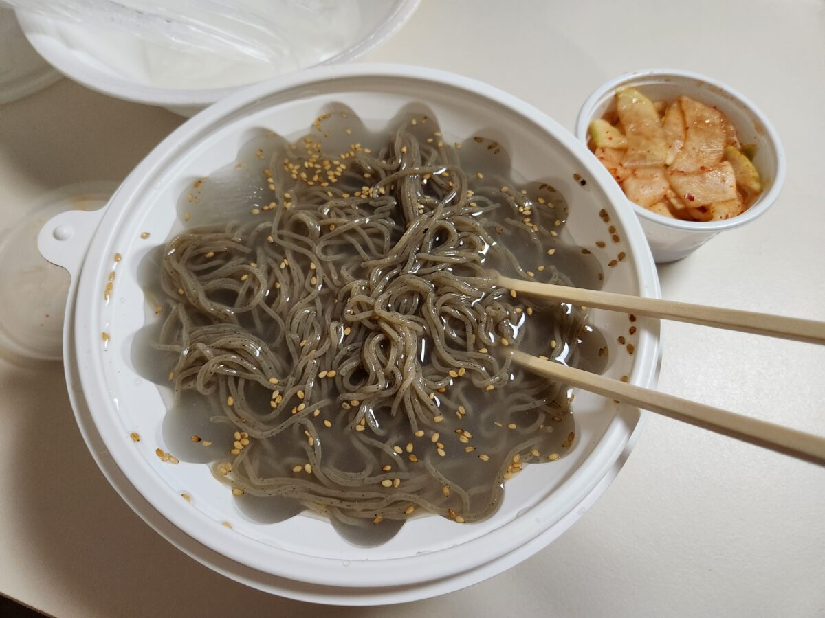 젓가락으로 메밀면을 들어 올리는 모습과 옆에 놓인 무김치.