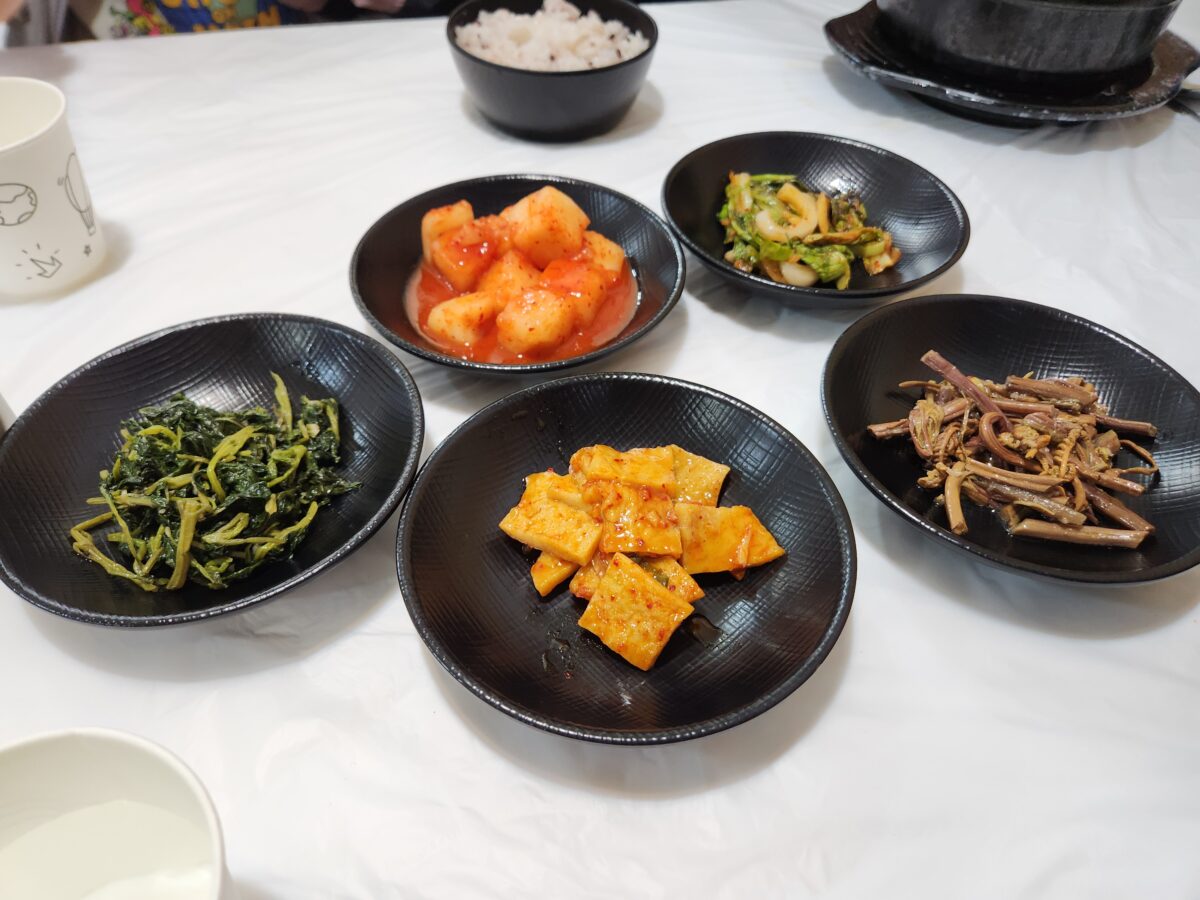 나물무침, 김치 등이 담긴 검은색 접시들이 테이블에 놓여있는 모습.