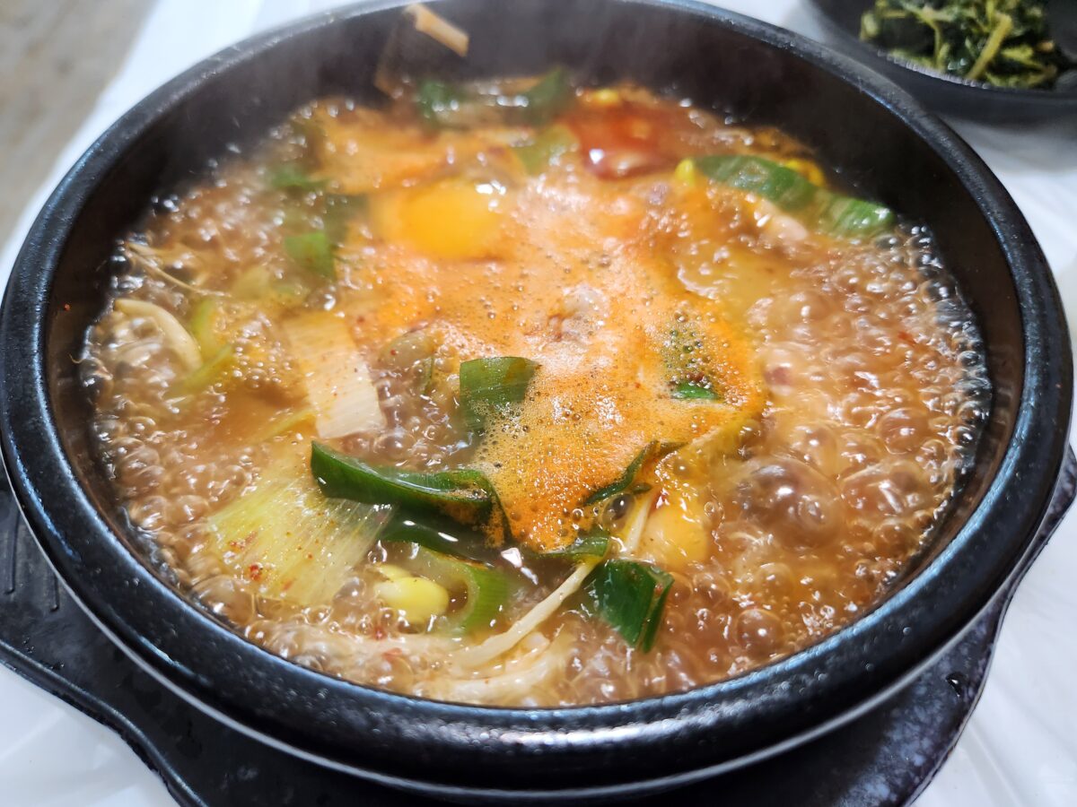 뚝배기 안에서 팔팔 끓고 있는 오징어해장국과 날계란 모습.