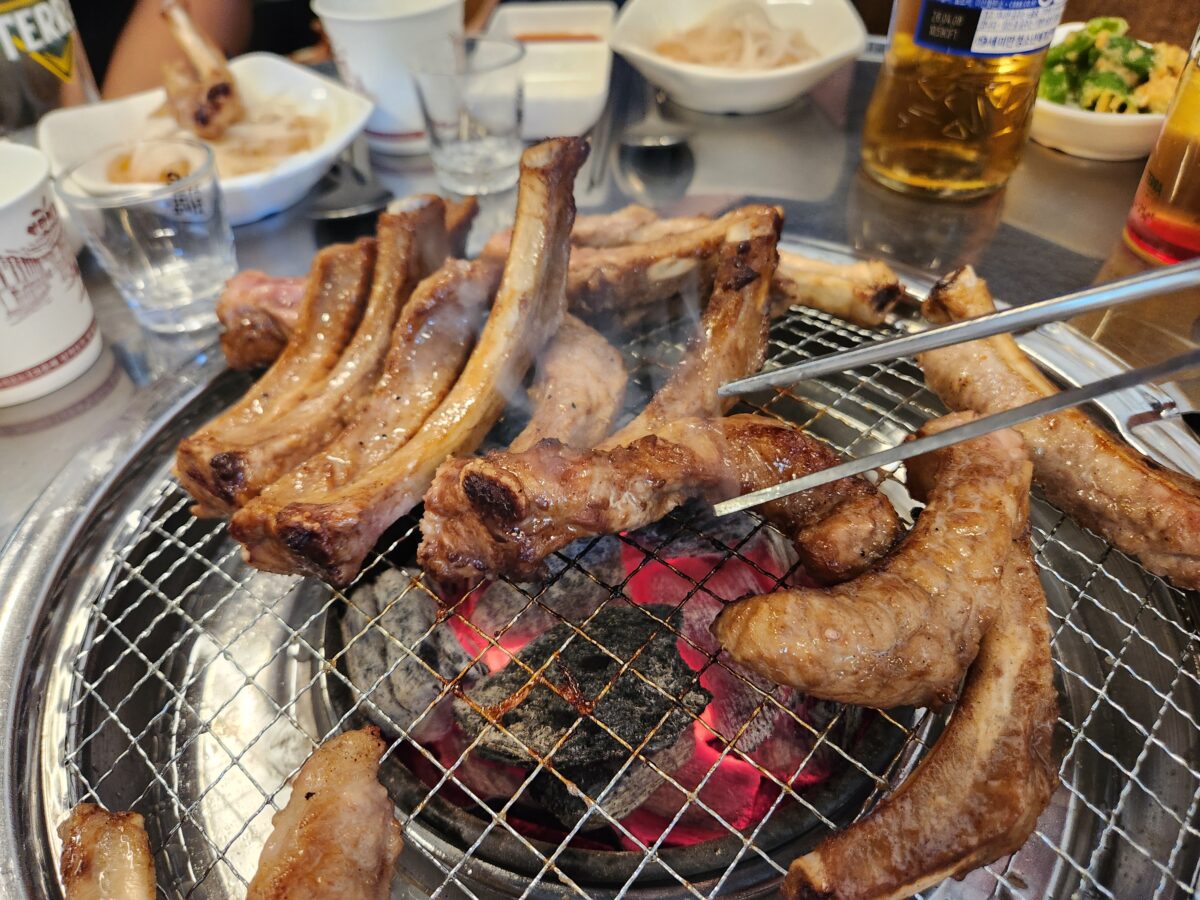 집게로 쪽갈비를 뒤집으며 숯불에 굽고 있는 근접 촬영.