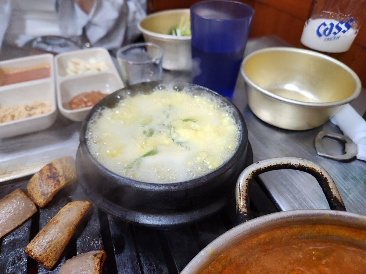 테이블 위에 놓인 뚝배기에 담긴 계란찜과 주변 고기집 상차림 모습.