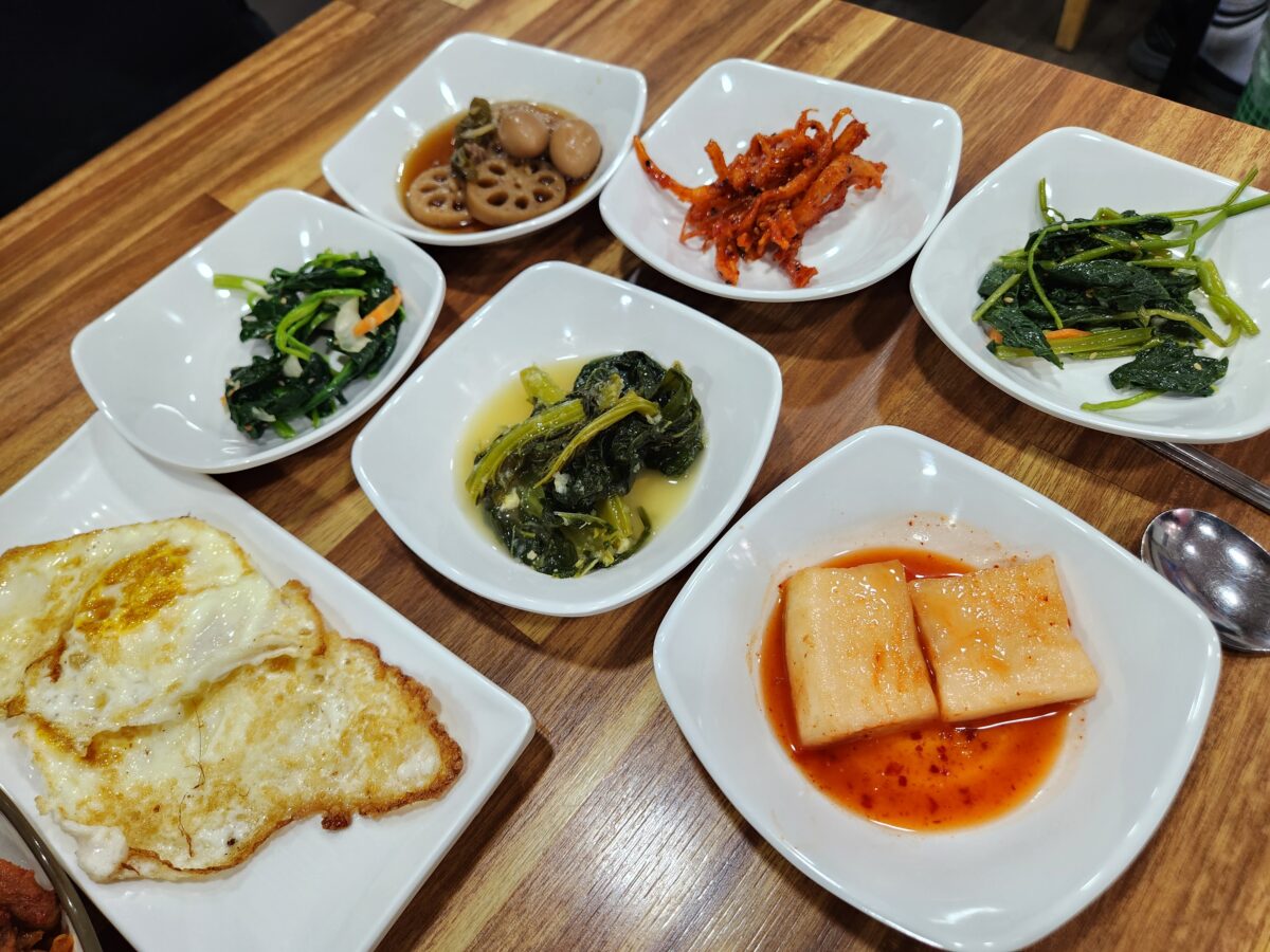 나물, 연근조림, 진미채, 갓 백김치 등 다양한 밑반찬이 놓인 식탁.