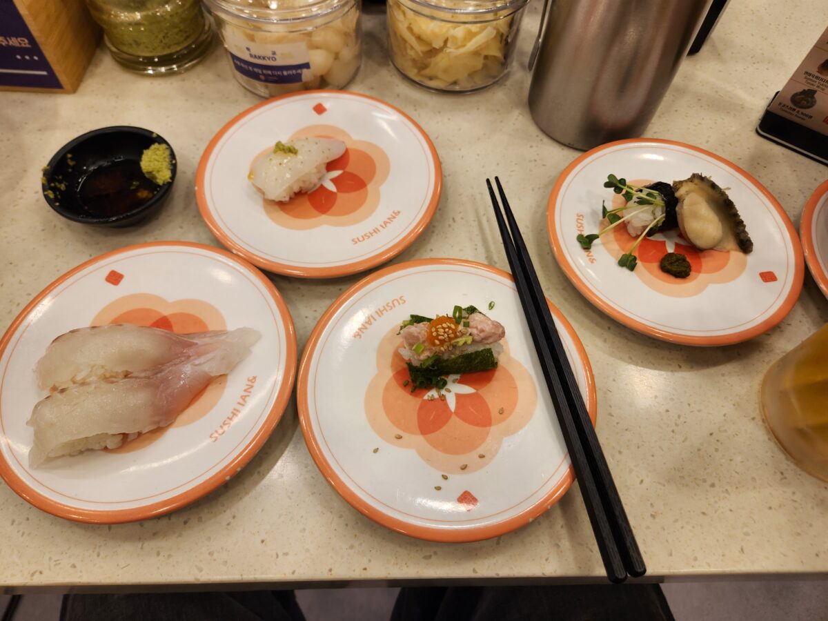 회전초밥집 테이블 위에 광어, 한치, 전복, 명란네기도로 초밥 접시들이 놓여 있는 모습.