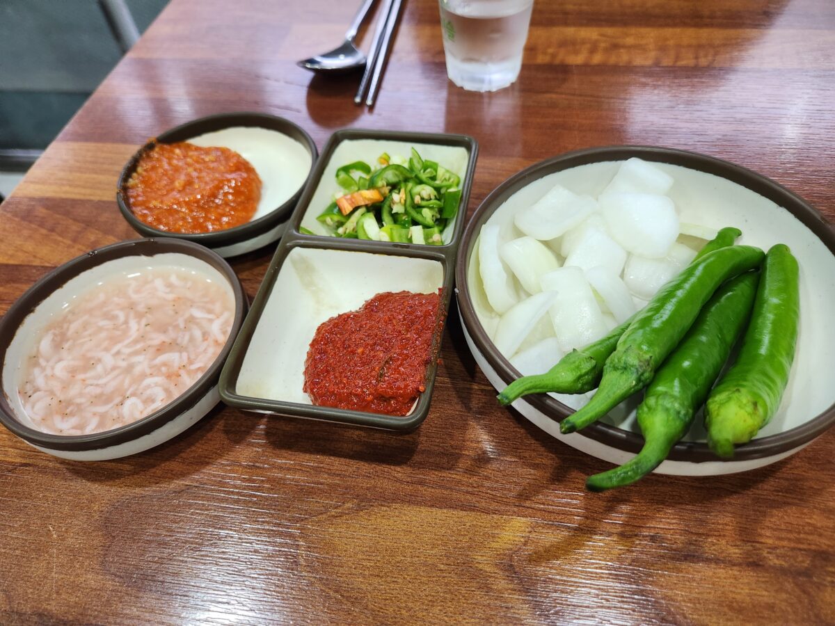 테이블 위에 놓인 소스류, 청양고추, 양파, 새우젓 등 밑반찬들