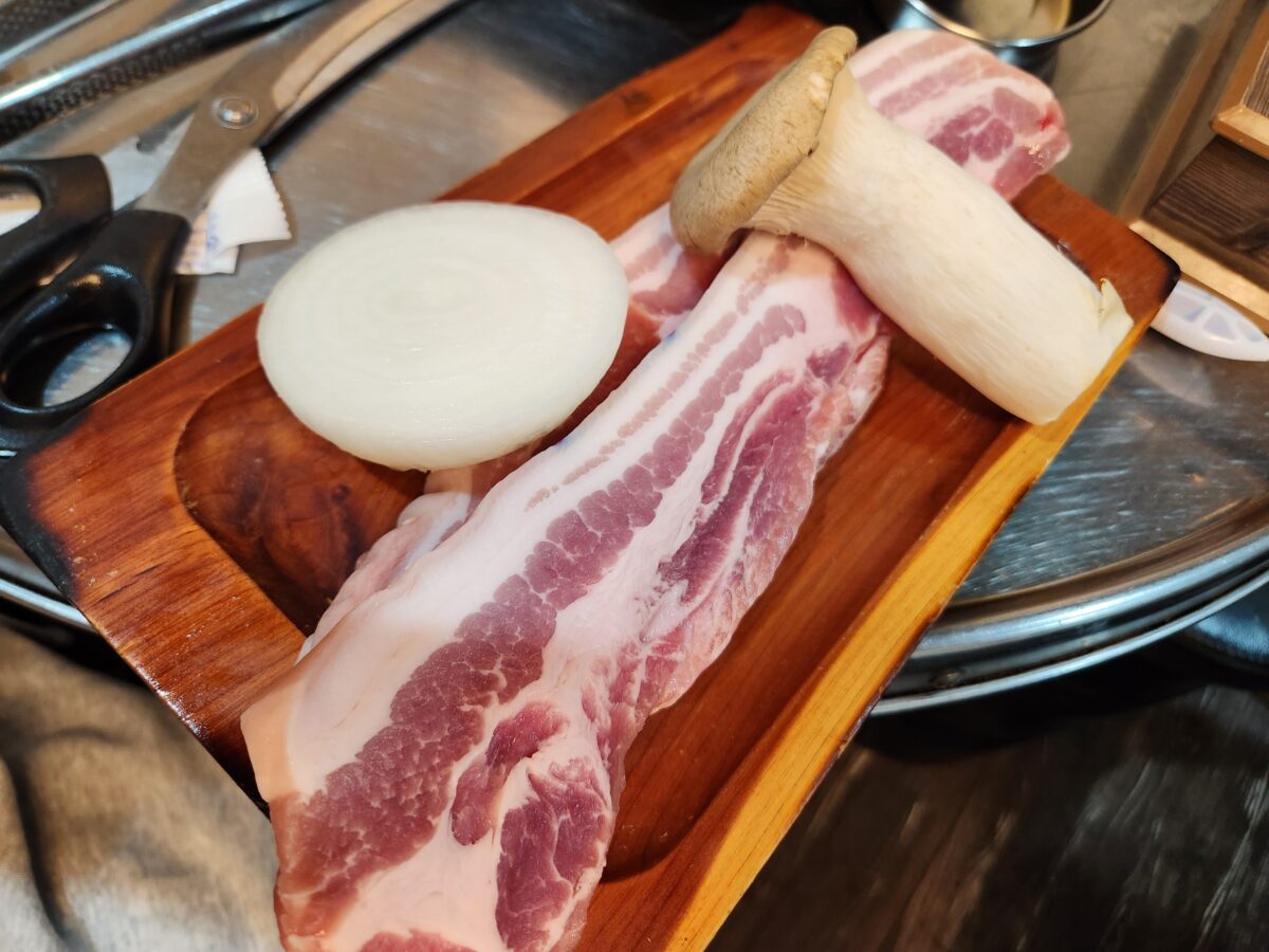 나무 도마 위에 올려진 생오겹살과 양파, 새송이버섯.