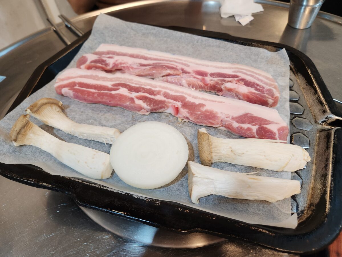 달궈진 불판 위에 올려진 오겹살, 양파, 버섯.