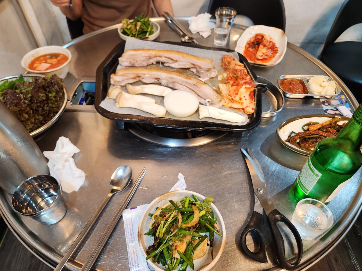 고기가 익어가는 불판과 밑반찬, 소주잔이 놓인 테이블 전체 모습.